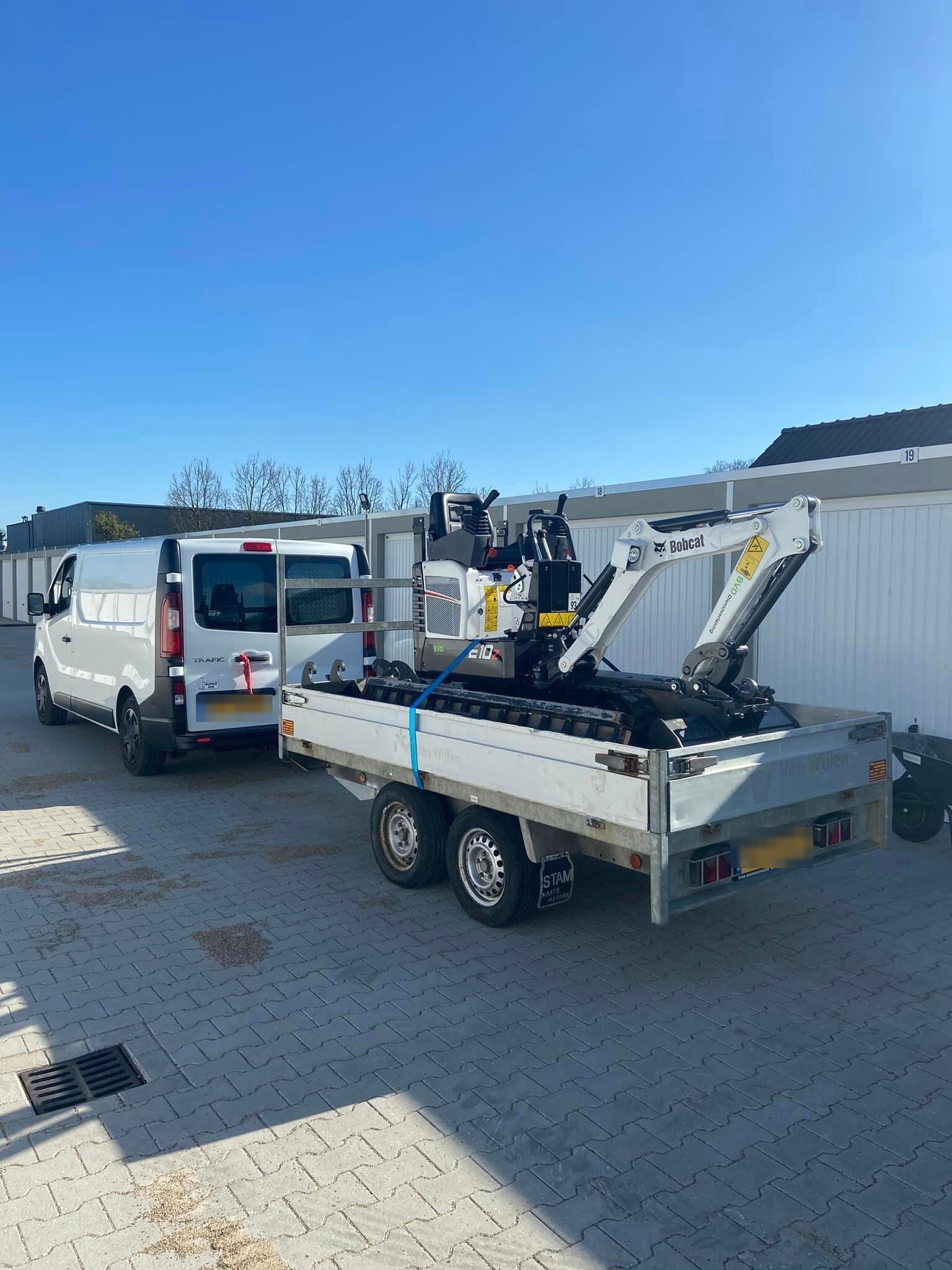 Bobcat minigraver op een aanhanger achter de bus