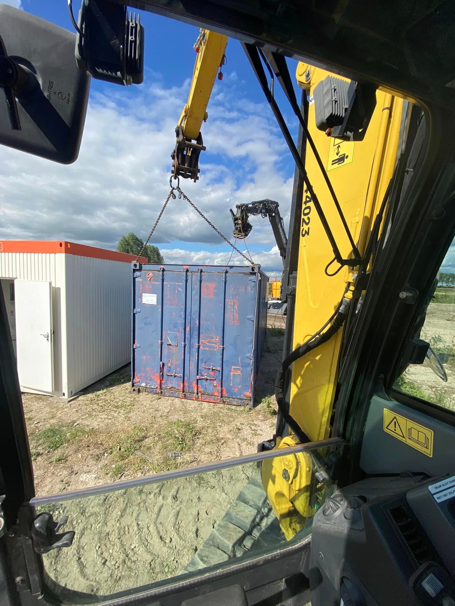 Zicht vanuit de cabine van een graafmachine die een container verplaatst