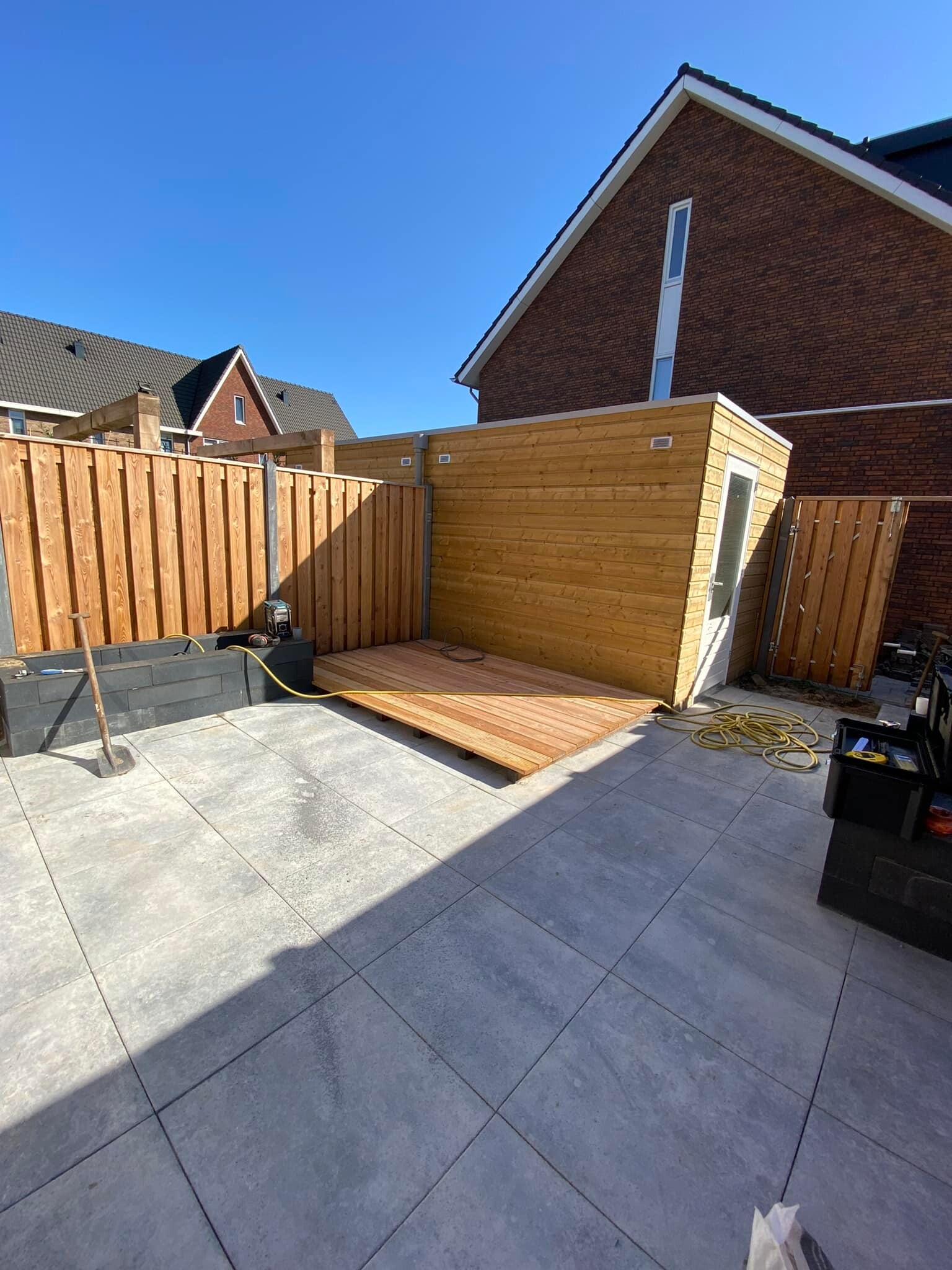 Nieuwe achtertuin met grote keramische tegels, houten schutting en berging