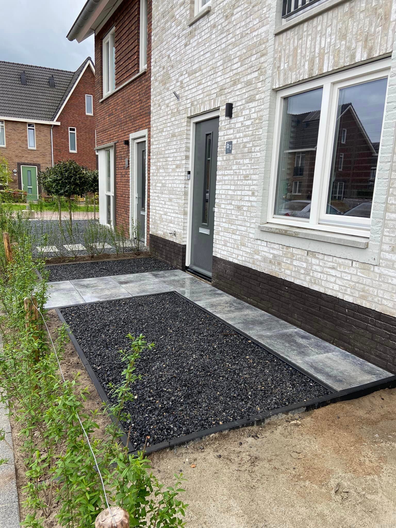 Voortuin met donker grind en lichte tegelrand naar de voordeur