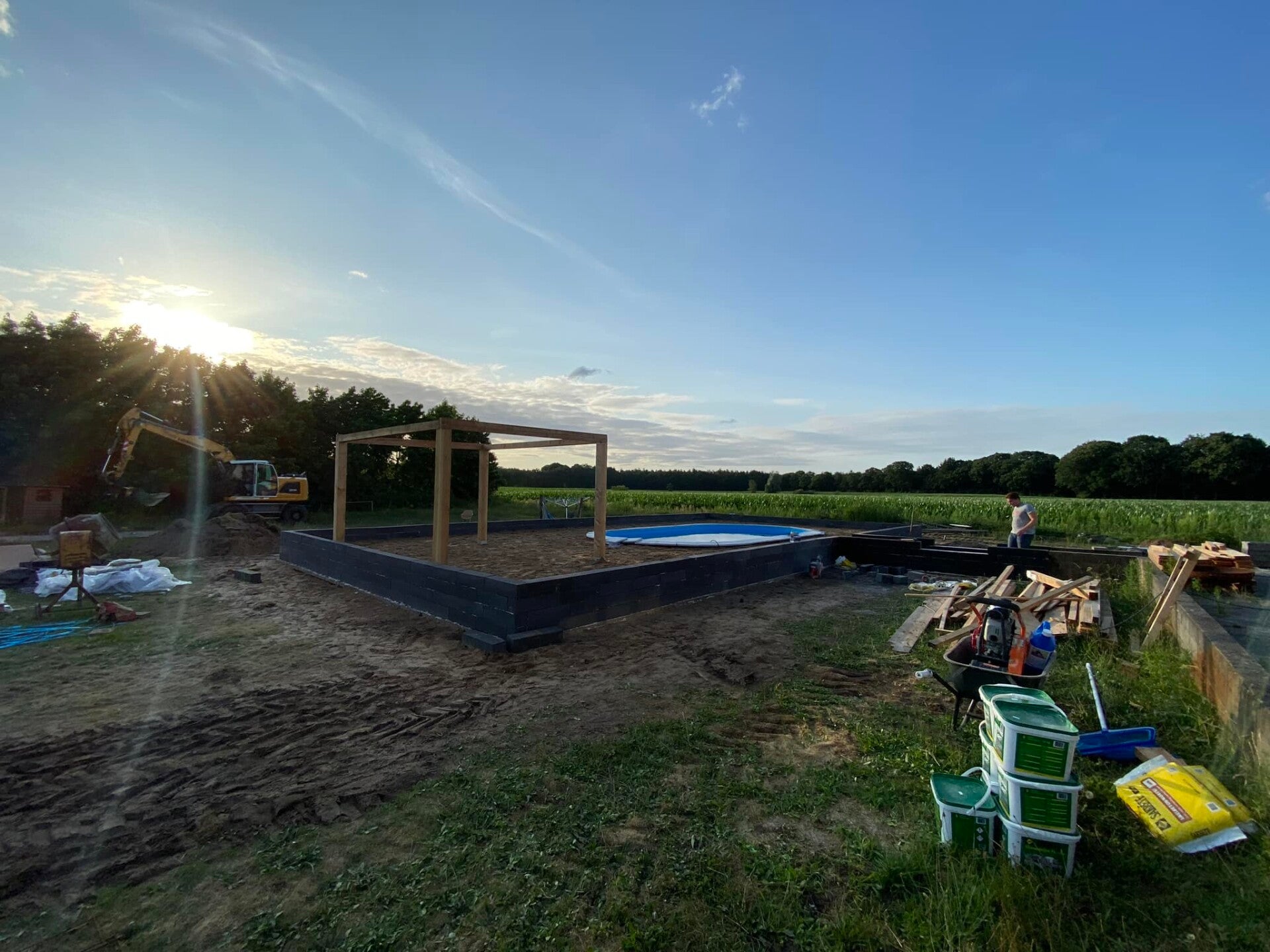 Achtertuin in aanleg met zwembadrand en houten overkapping bij zonsondergang